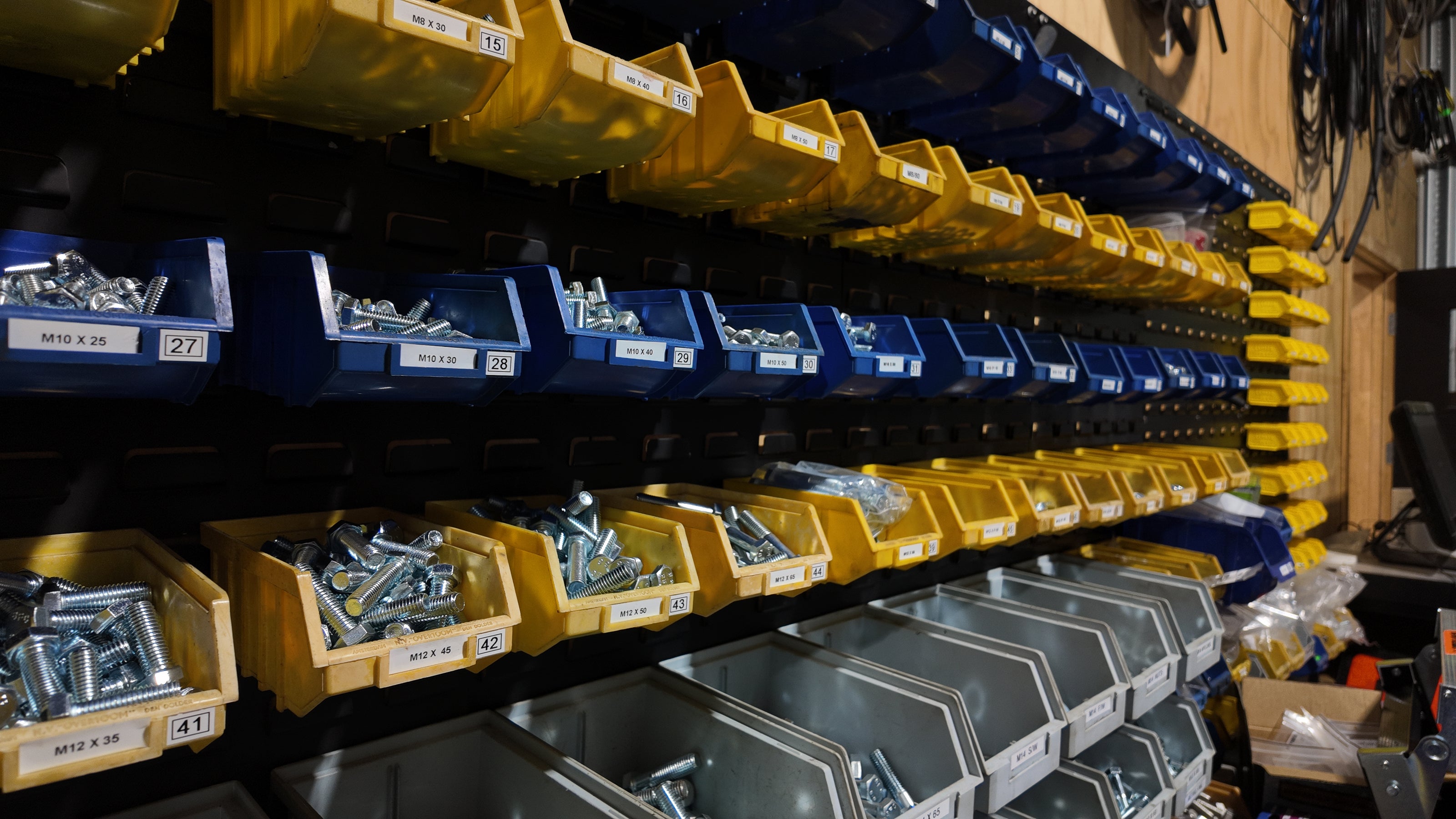 Industrial shelving units stocked with organized hardware bins containing screws, bolts, and nuts, with labels on each compartment.