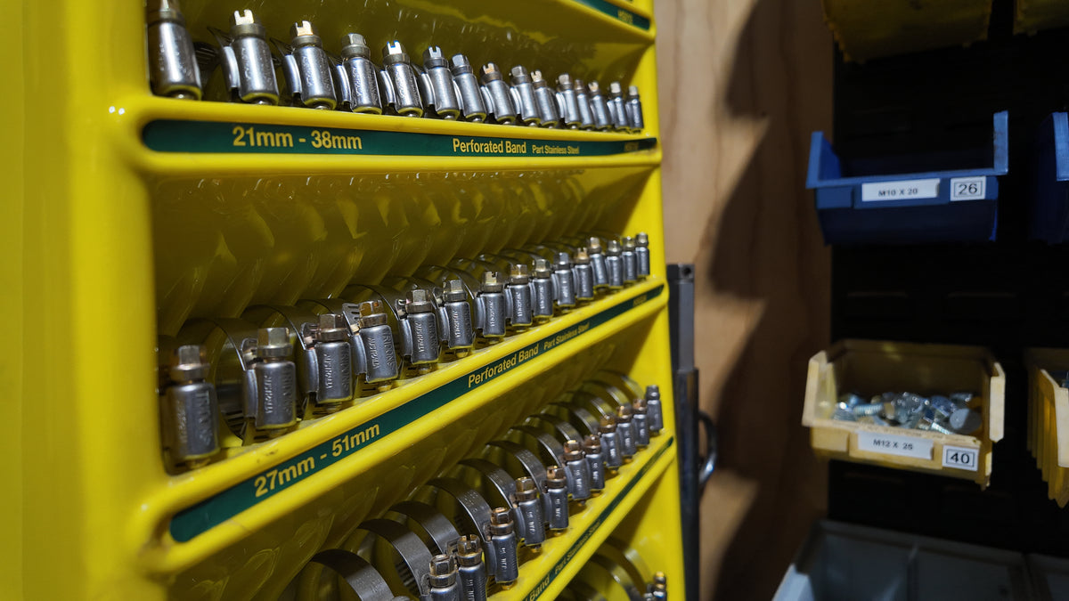 A yellow metal tool rack filled with silver perforated band saw blades, photographed in a workshop setting with storage bins in the background.