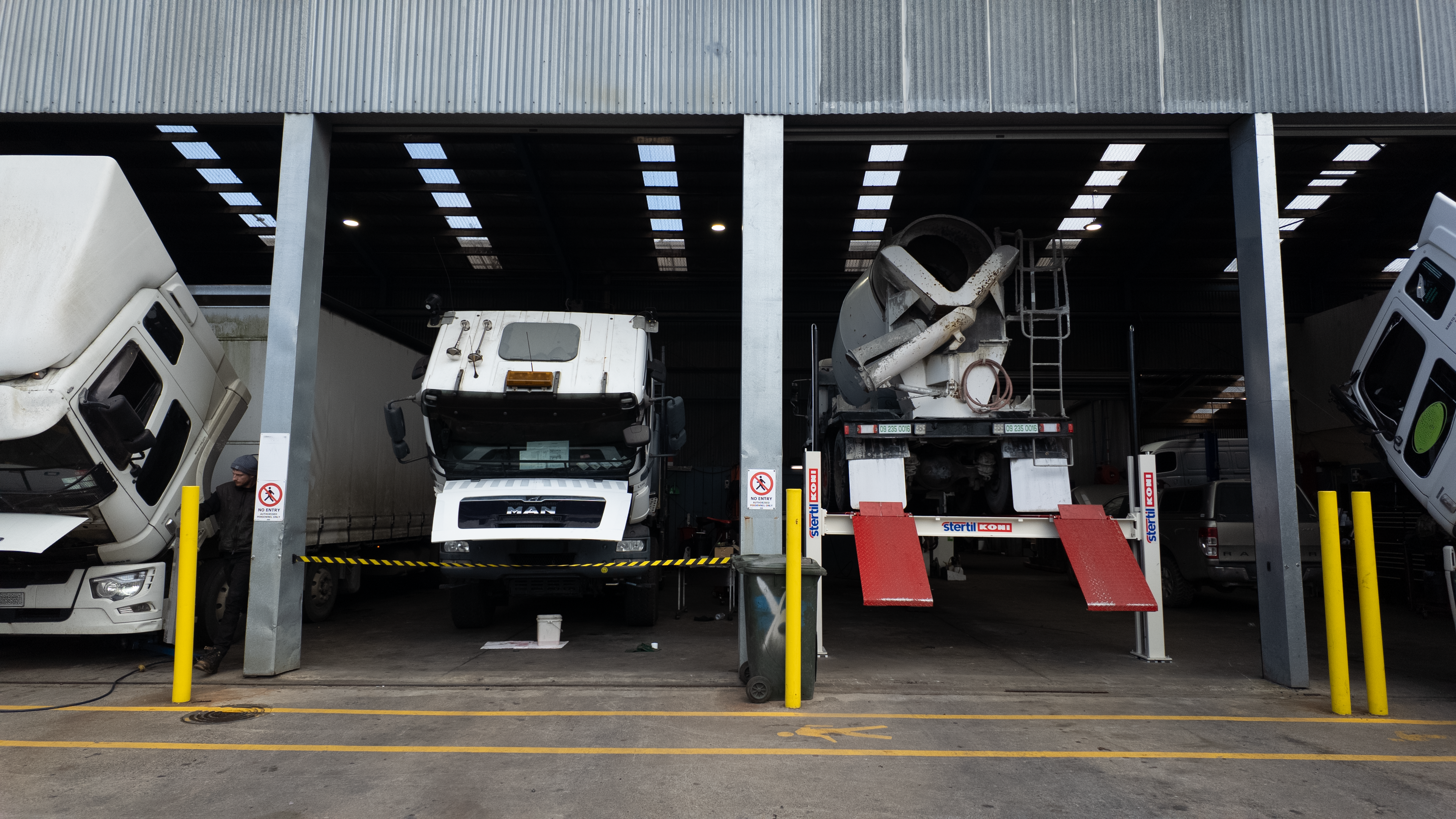 A large industrial garage or warehouse with multiple trucks parked inside. A white MAN box truck is centered in the middle bay, with other trucks partially visible on both sides.