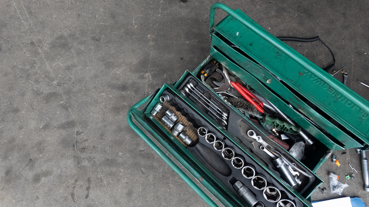 An open green metal tool box filled with various hand tools, including sockets, wrenches, and screwdrivers, placed on a gray concrete floor. Diesel Workshop 1924 pukekohe auckland