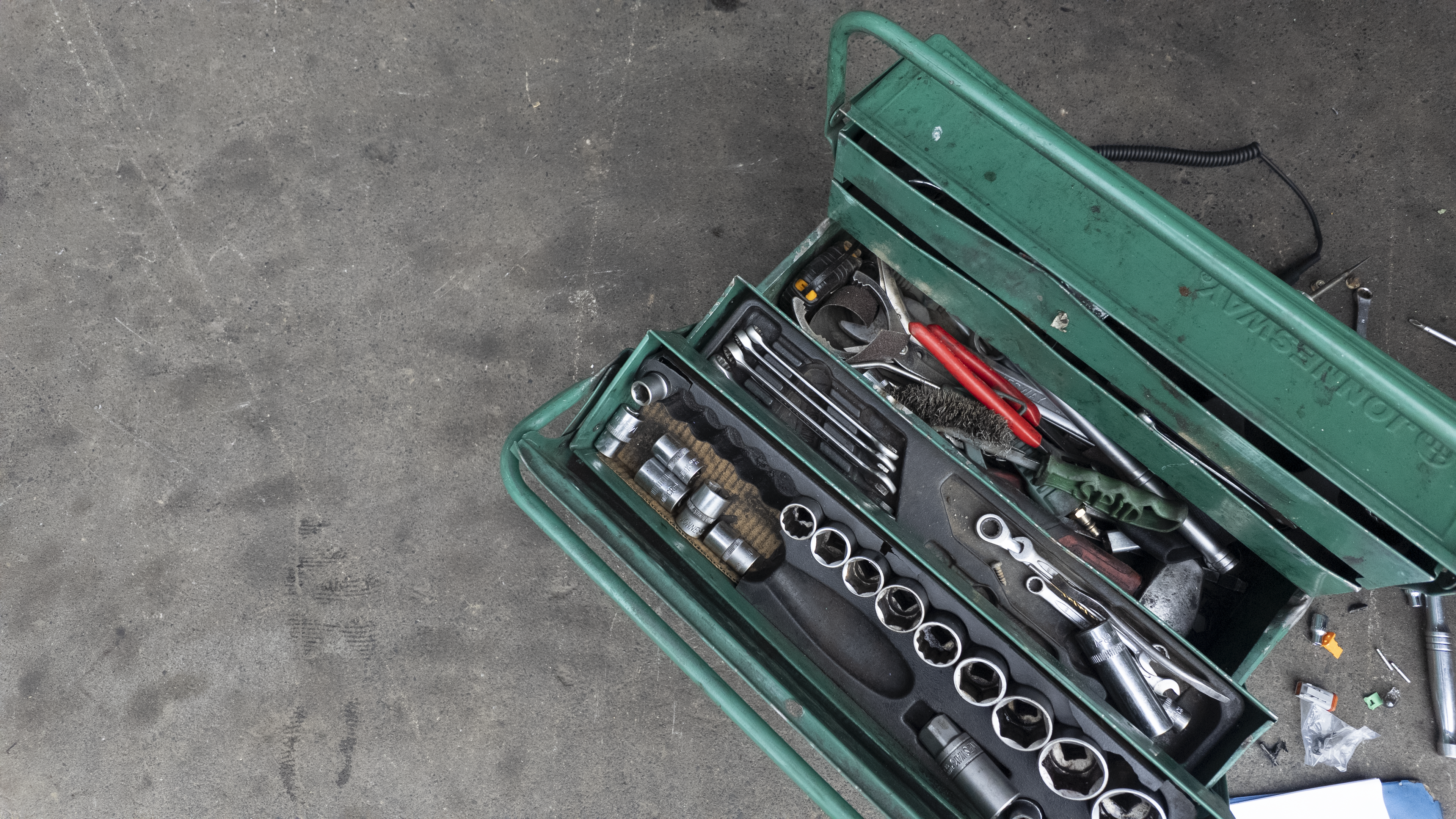 An open green metal tool box filled with various hand tools, including sockets, wrenches, and screwdrivers, placed on a gray concrete floor. Diesel Workshop 1924 pukekohe auckland